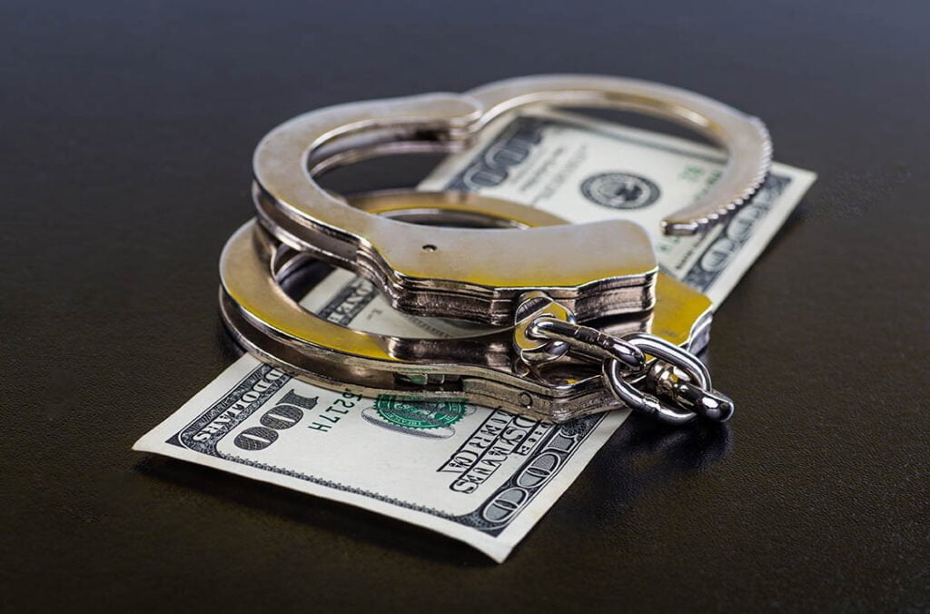 Handcuffs rest on top of a 100 dollar bill on a black surface